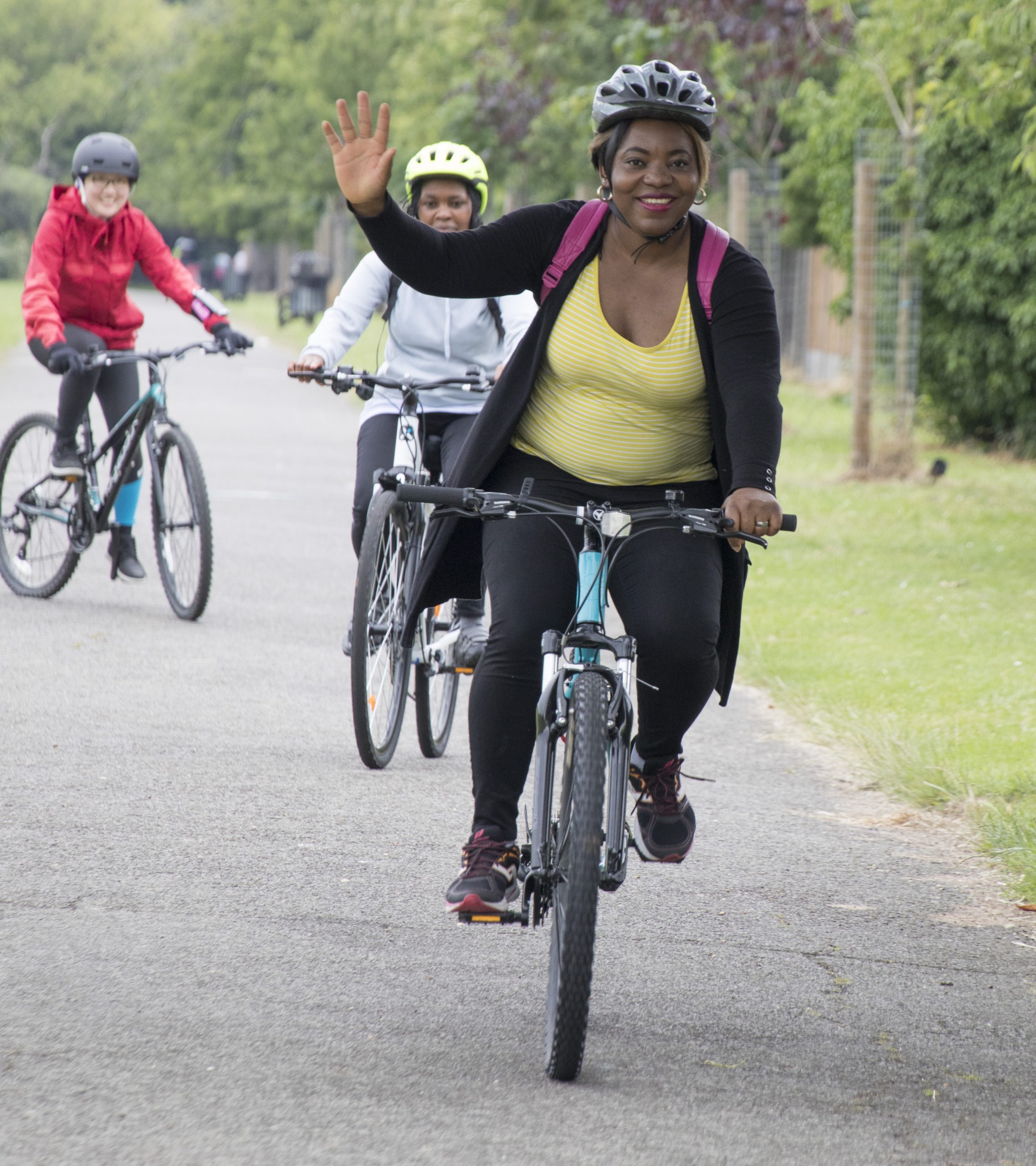 A woman waves at the camera whilst riding a bike