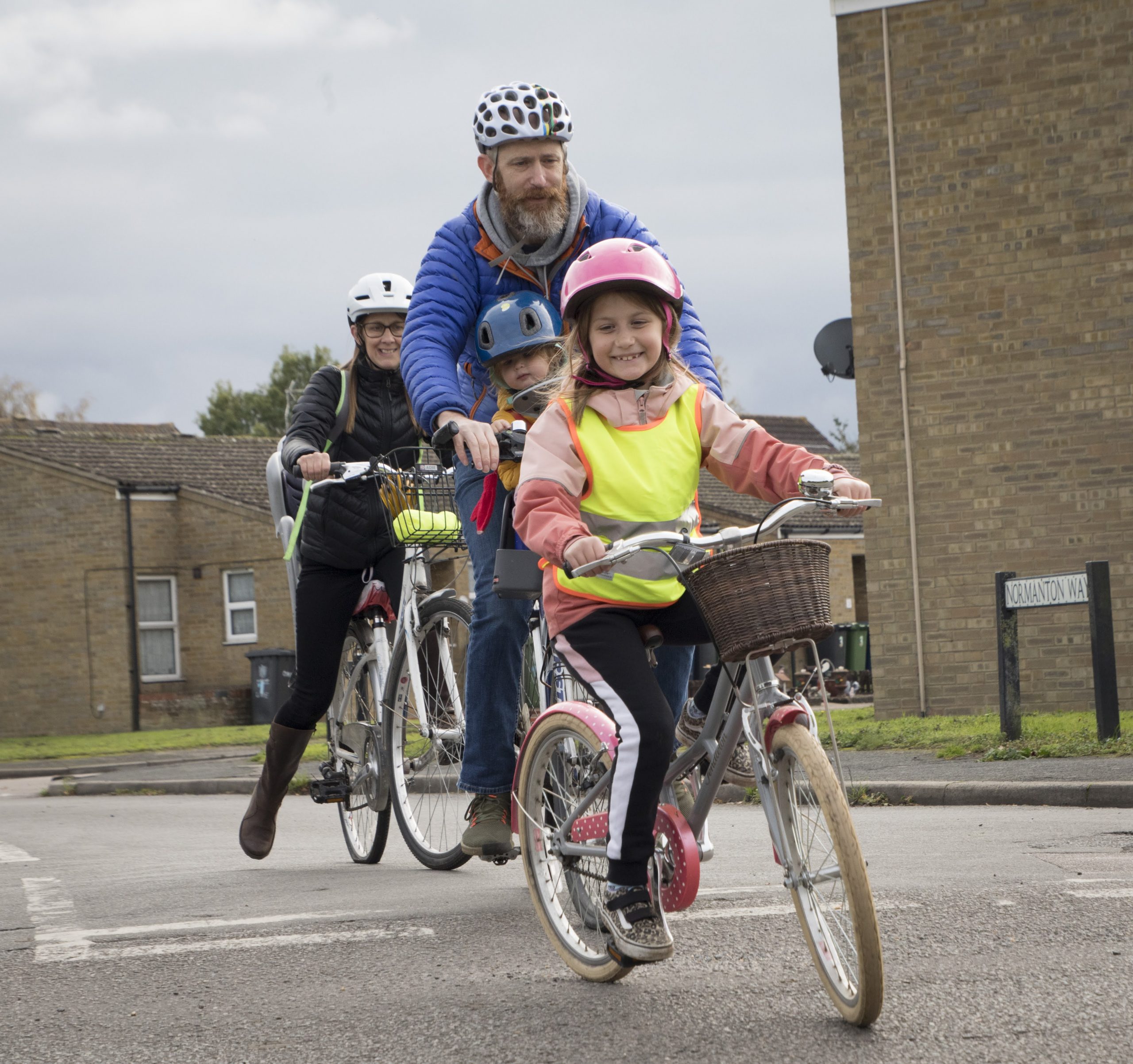 A young girl smiling on a bike with her dad and mum behind her on bikes