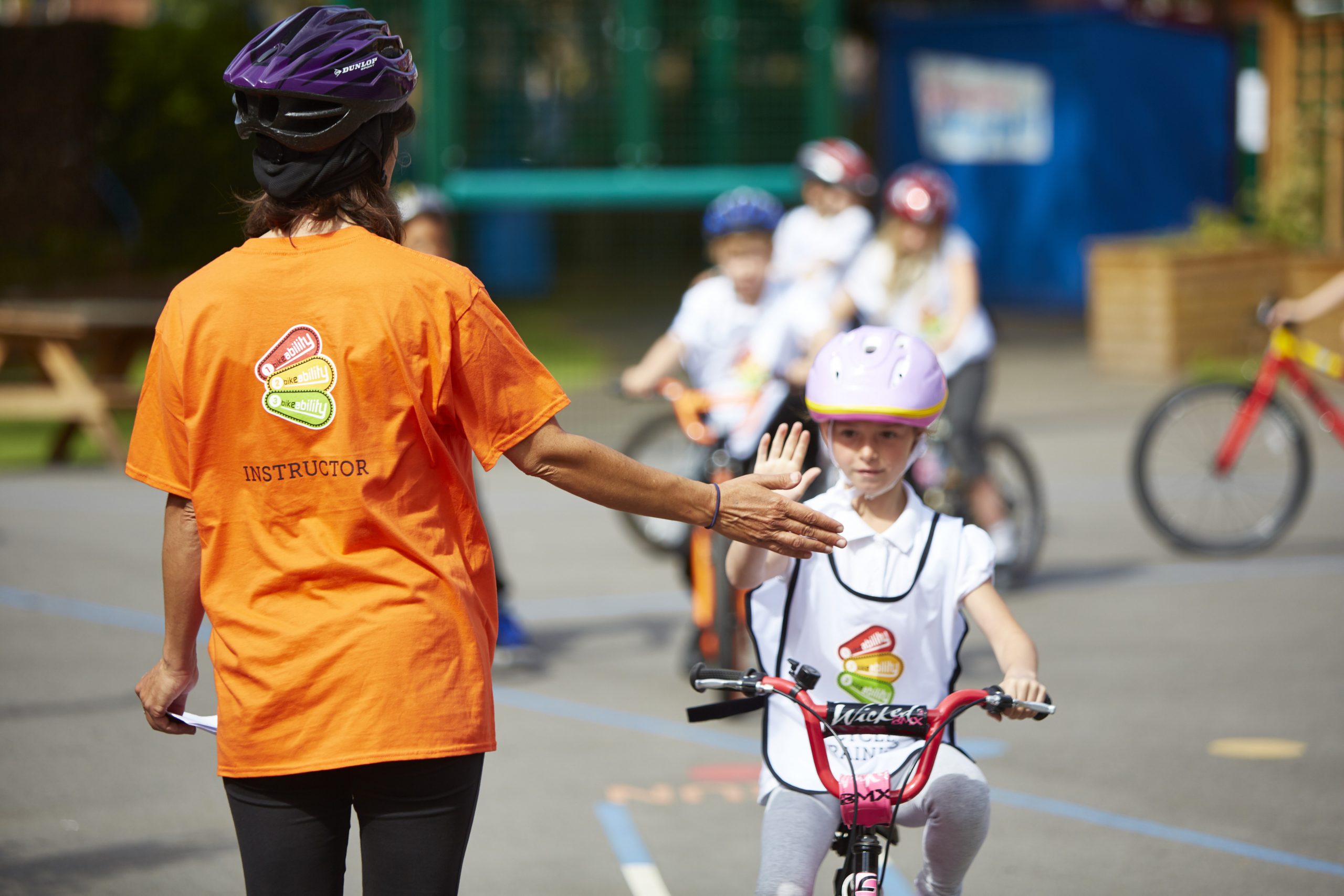 A Bikeability Professionals instructor high fiving a young girl on a bike