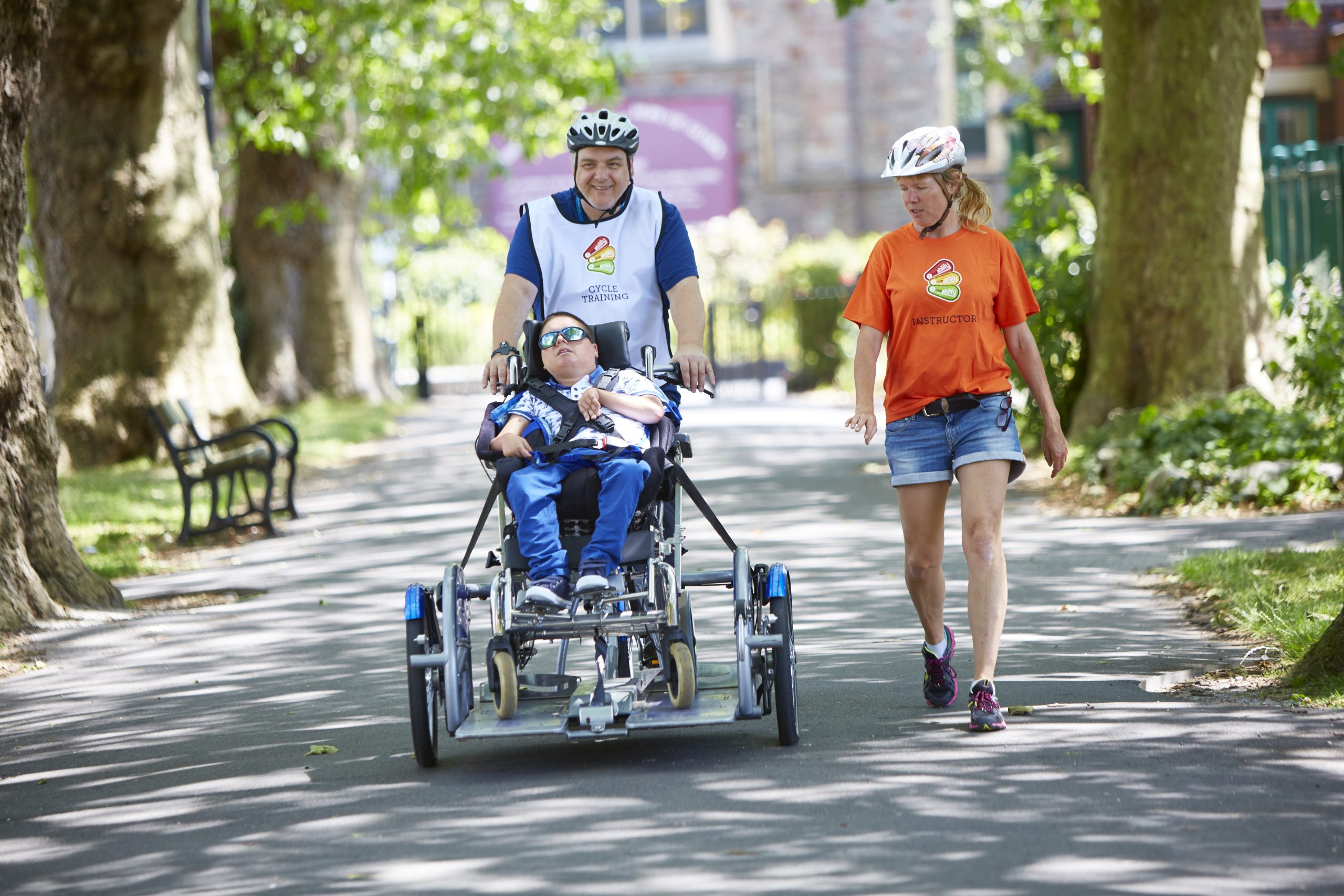 A child on an adapted bike being ridden by a man with a female instructor walking beside them