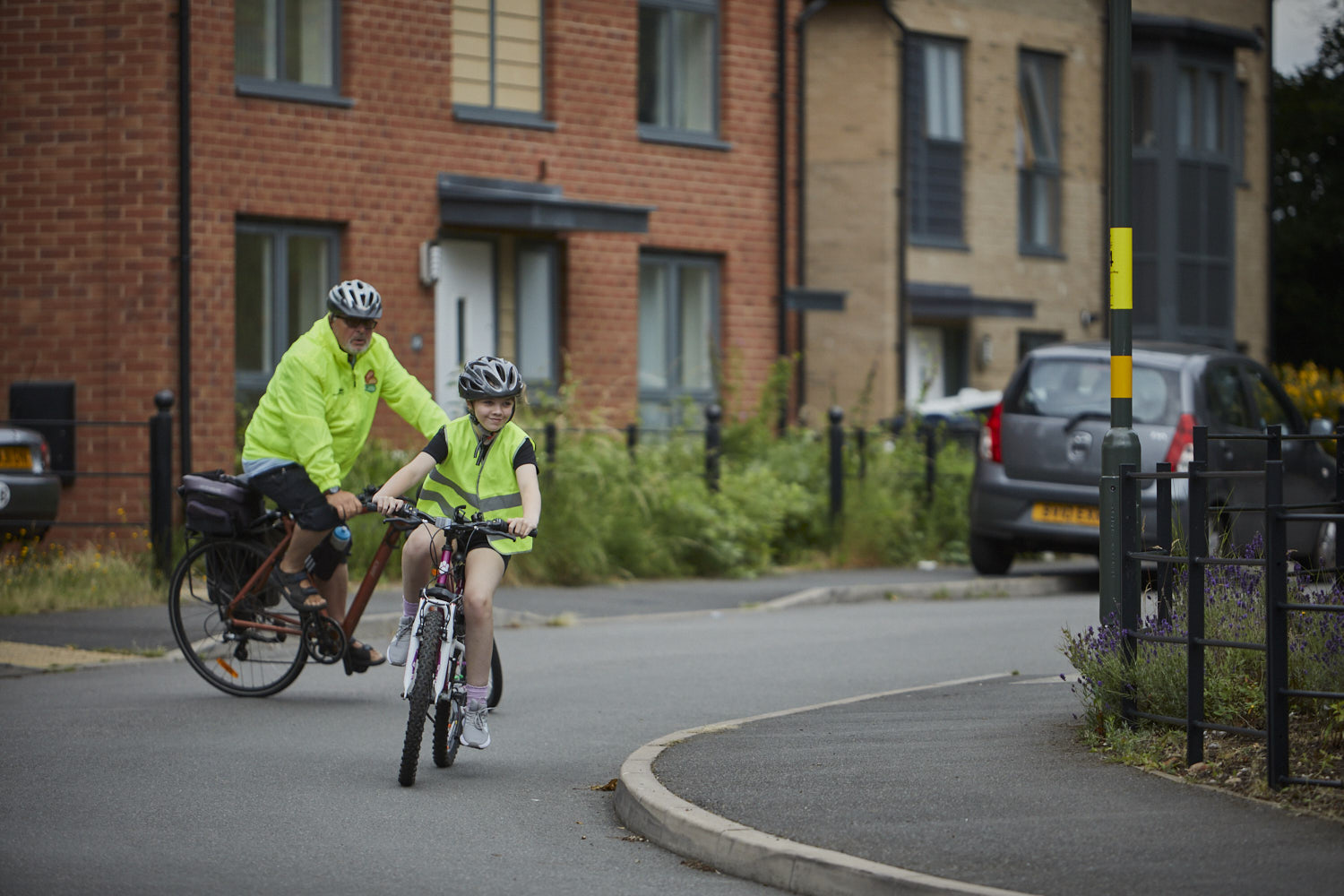 Young girl on bike in high vis with Bikeability instructor behind her