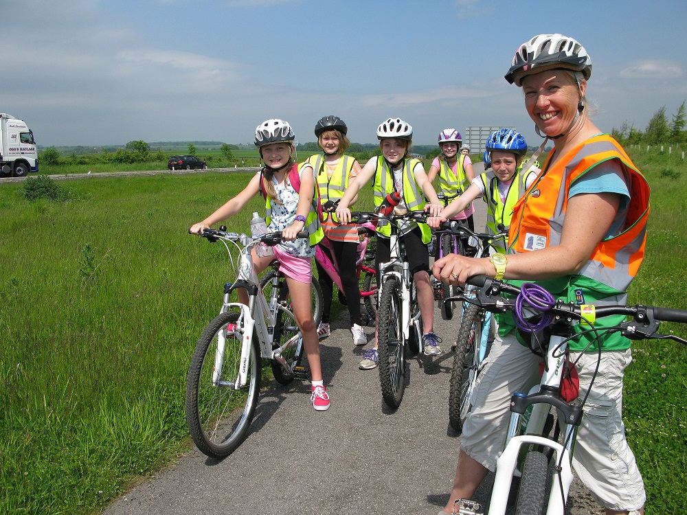 A woman on a bike stands in front of a group of girls on bikes