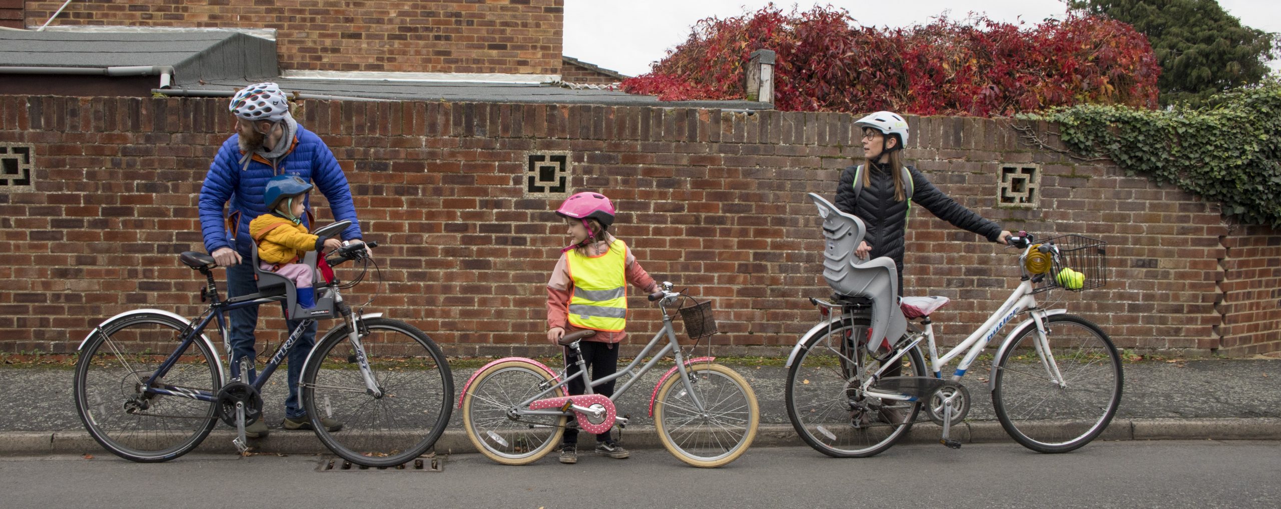 A man, child and woman stood next to their bikes looking behind them. The man has a toddler in a seat on his bike.